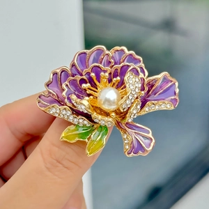 Detail van grote paarse pioenroos broche met parelmoer midden en strass op goud
