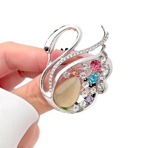 Elegant silver swan brooch with colorful crystals and opal stone held in hand