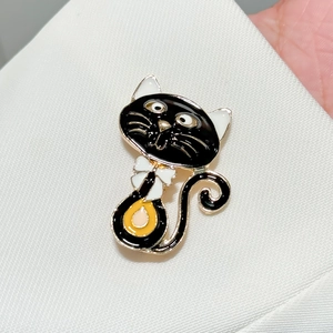 Broche chat en émail noir avec bordure dorée et nœud blanc sur tissu blanc