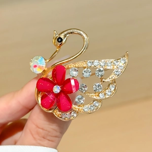 Elegante broche de cisne dorado con cristales brillantes y detalle de flor roja