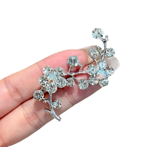 Elegant floral silver brooch with shimmering crystals and iridescent stones held in hand