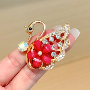 Detalle de broche de cisne dorado con pétalos rojos y cristales blancos brillantes