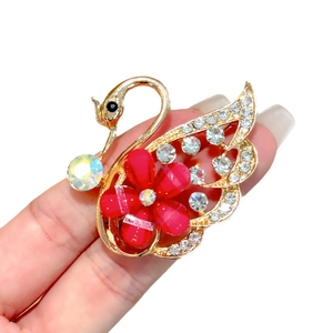 Broche de cisne dorado con pétalos rojos y pedrería sostenido a mano sobre fondo blanco