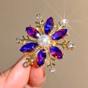 Detailed close-up of a golden snowflake brooch with blue crystals and a central pearl