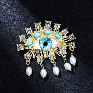 Detailed view of evil eye brooch with blue stones, rhinestones and pearl tassels