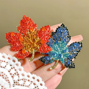 Detailed macro view of maple leaf brooch with vibrant orange and blue green rhinestones