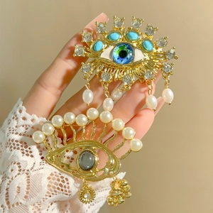 Evil Eye gold brooches with blue crystals and pearls held in hand for elegant styling