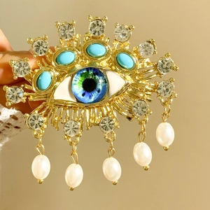 Detailed view of evil eye brooch with blue stones, rhinestones and pearl tassels