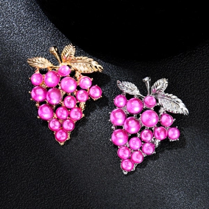 Elegant gold and silver grape brooches with pink pearls on a premium black leather surface