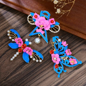 Detail of enamel dragonfly and butterfly brooches with faux pearls on wooden base