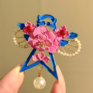Macro detail of a floral brooch with pink enamel petals, blue leaves and a pearl drop
