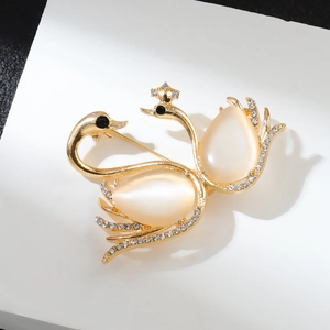 Elegant gold twin swan brooch with white opal cat-eye stones and crystal accents