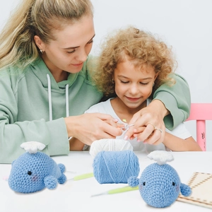 DIY crochet kit showing adult and child crafting two blue knitted whale plush dolls together