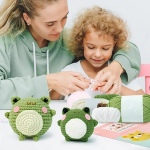 Detail of crochet kit showing green frog plush toys and colorful yarn for DIY crafting