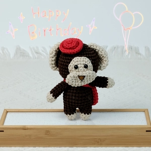 Close-up of a handmade crochet monkey plush with red hat and scarf on a wooden stand