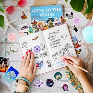 Flat lay of gothic magic stickers and summer beach props on a travel journal