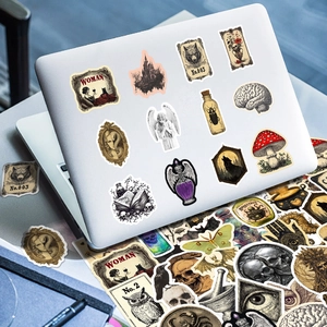 Close-up of vintage gothic apothecary stickers on a white laptop with dark occult motifs