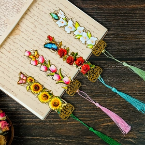 Detailed set of four hollow metal flower bookmarks with silk tassels on a vintage book