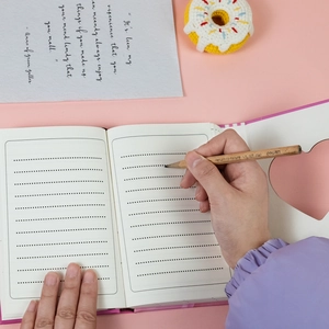 Close-up of pink heart cutout notebook with lined inner pages and a wooden pencil