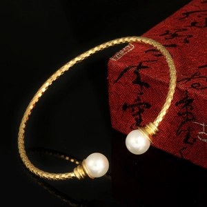 Gold plated open bangle with white pearls and diamond-textured pattern on black surface