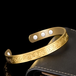 Detail of gold magnetic therapy cuff bracelet featuring Greek Key pattern on black leather