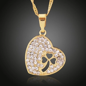 Close-up of heart-shaped gold pendant featuring pavé crystals and a clover cutout