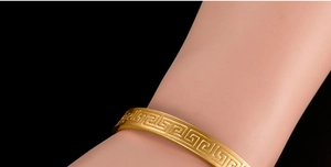 Close-up of 18K gold plated bracelet with Greek Key pattern against a black background