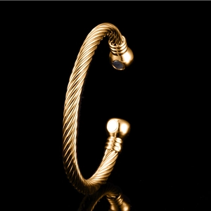 Goldenes gedrehtes offenes C-Armreif-Armband mit magnetischen Enden auf schwarzem Hintergrund