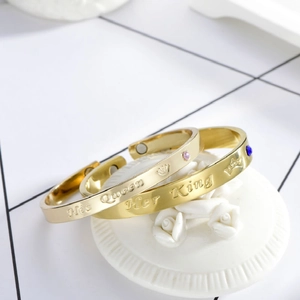 Detail of gold C-shape couple bracelets with His Queen and Her King crown engravings
