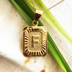 Dettaglio macro della collana quadrata placcata oro 18K con lettera F su foglia