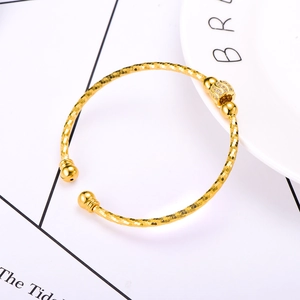 Golden open bangle with textured band and zircon-inlaid beads on white ceramic tray