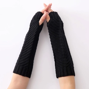 Detail of black knit fingerless arm warmers showing thick cable stitch texture and thumb hole