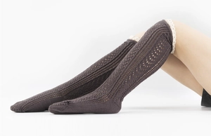 Close-up of dark brown cable knit leg warmers featuring white lace trim and hollowed patterns
