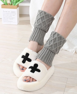 Detail of grey knitted leg warmers with diamond pattern and plush white slippers