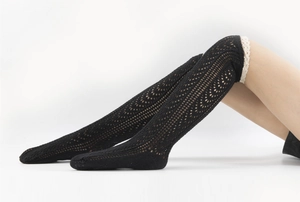 Detailed view of black knitted hollow-out leg warmers with white lace trim detail