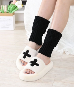 Close-up of black diamond knit leg warmers paired with plush cross-pattern slippers