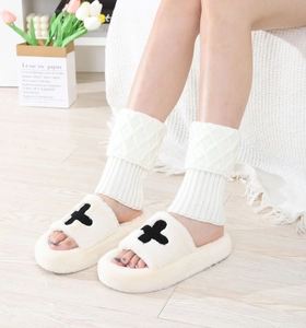 Detail of white cable knit leg warmers paired with cozy cream plush slippers on floor
