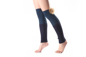 Detail of two-tone knit leg warmers with brown pom poms on textured ribbed fabric