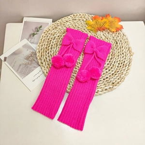 Detail of fuchsia knit leg warmers with ribbon bows and soft plush pom-poms on straw mat