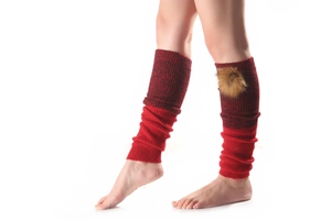 Close-up of red gradient knit leg warmers with detachable brown faux fur pom poms