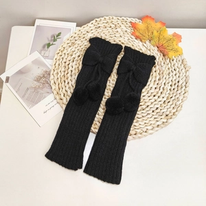 Close-up of black knitted leg warmers featuring cute bows and hanging fluffy pom-poms