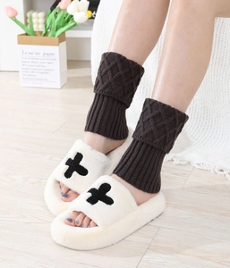 Close-up of brown diamond-patterned knit leg warmers paired with plush cross slippers