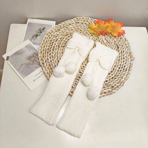 Detail of white cable knit leg warmers featuring fuzzy pom-poms and cute bow accents