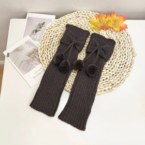 Detail of dark brown knit leg warmers with bow and plush pom-poms on a rustic mat