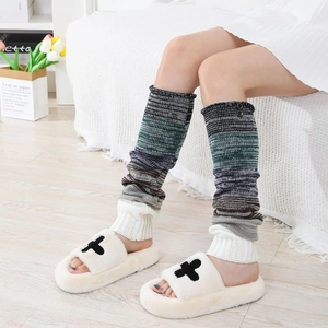 Détail de jambières en maille rayée avec des chaussons en peluche croisés sur le parquet