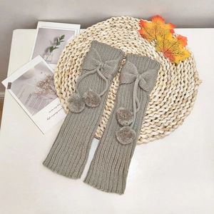 Detailed knit texture of gray leg warmers with decorative bows and plush pom-poms