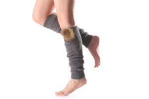 Detail of grey knitted leg warmer with fluffy raccoon fur ball and soft texture
