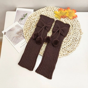 Detail of dark brown knit leg warmers with bow and fluffy pom-poms for kids