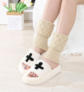 Close-up of beige diamond-knit leg warmers paired with plush white slippers on wood floor
