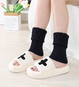 Detail of navy knit leg warmers and plush slippers on wooden floor in a cozy setting